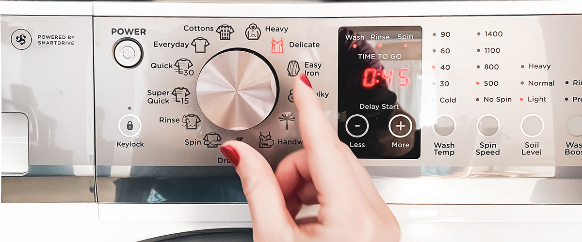 Hand with painted nail adjusts a washing machine dial