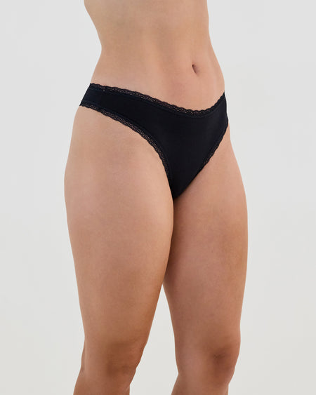 Model wears Stretch Cotton Thong in BLACK. On body side view