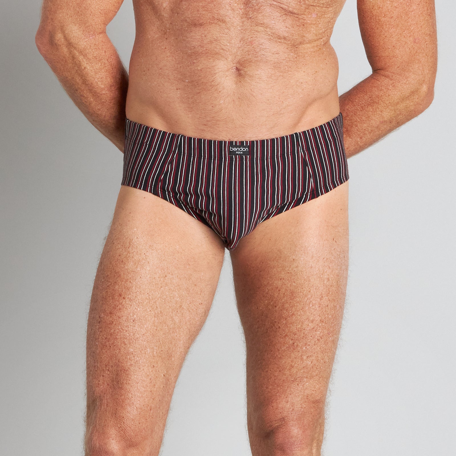 Model wears Cotton Stretch Mens Brief in BLACK/RHUBARB STRIPE. On body front view