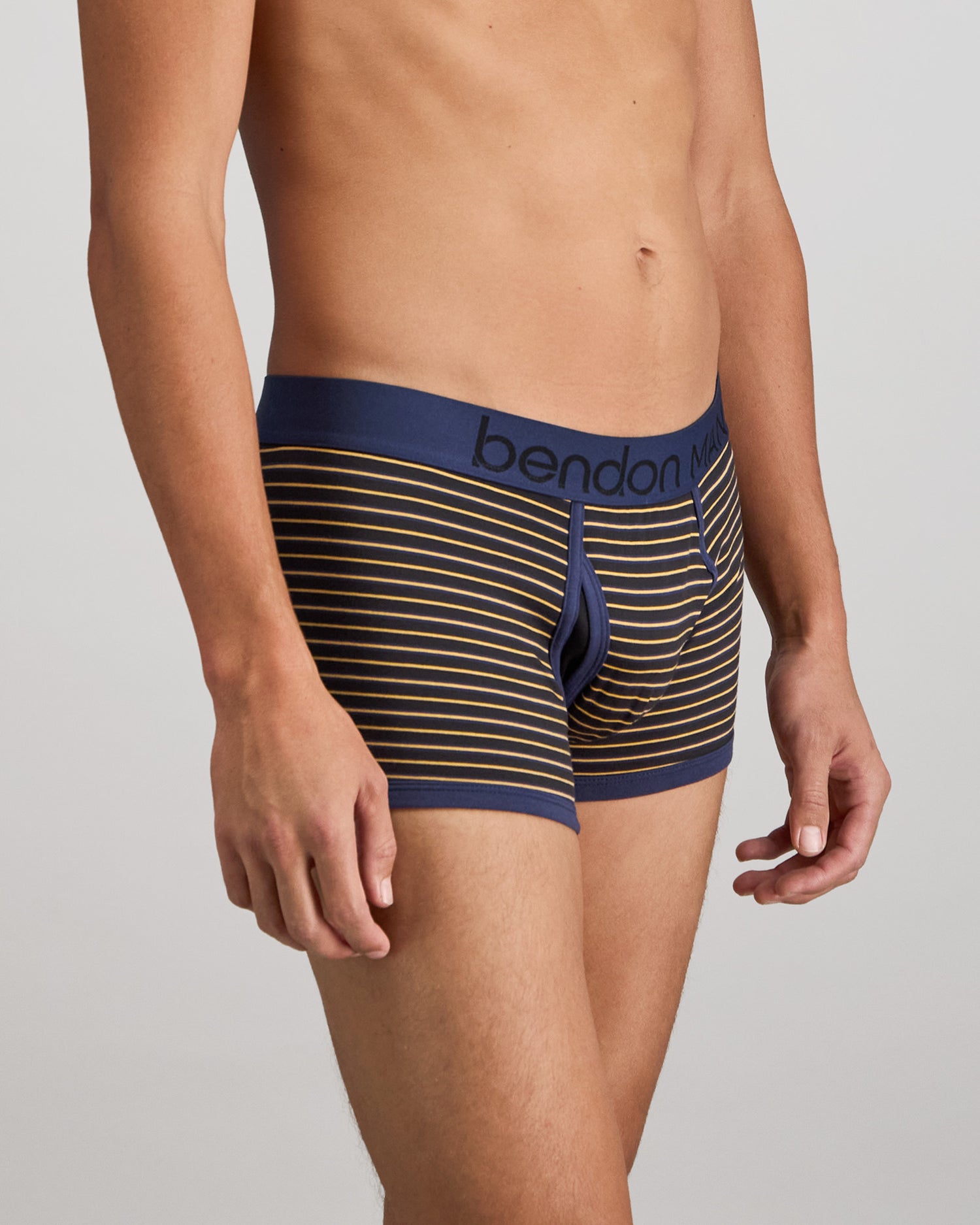 Model wears Bold Stripe Mens Trunk in BLACK/OAK BUFF STRIPE. On body side view