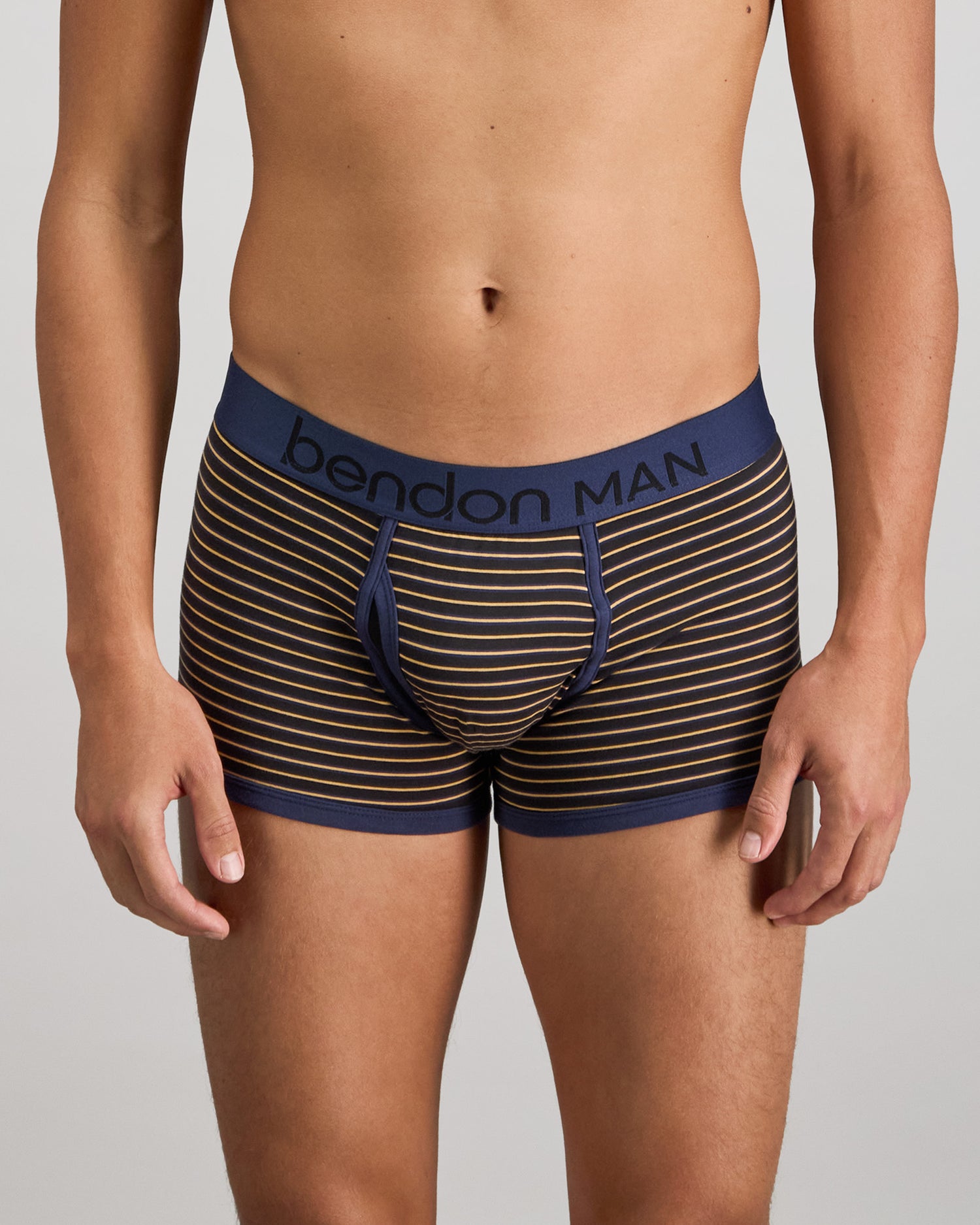 Model wears Bold Stripe Mens Trunk in BLACK/OAK BUFF STRIPE. On body front view